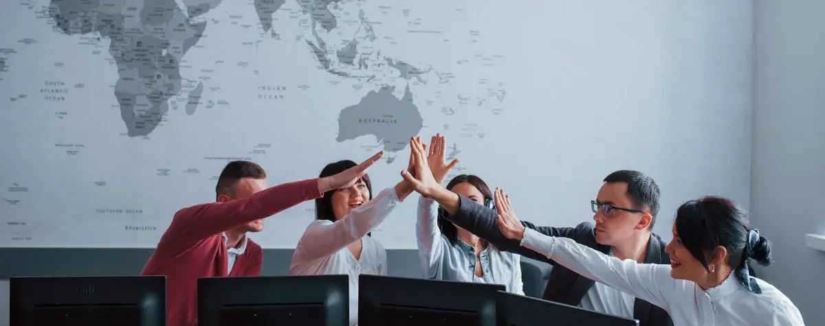 Colleagues sharing a high five across their desks in front of a wall-size world map