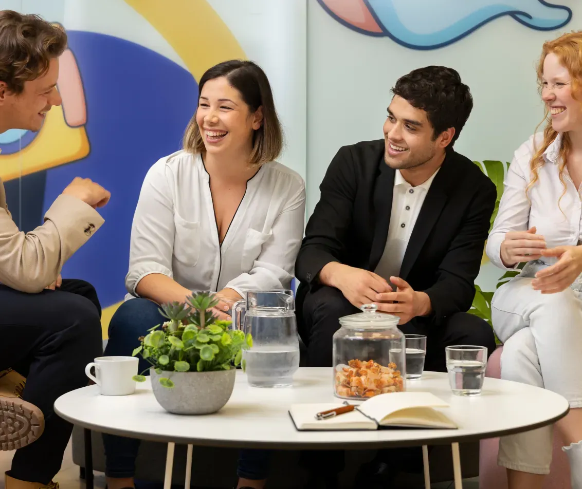 Four smiling team members talking around a low table