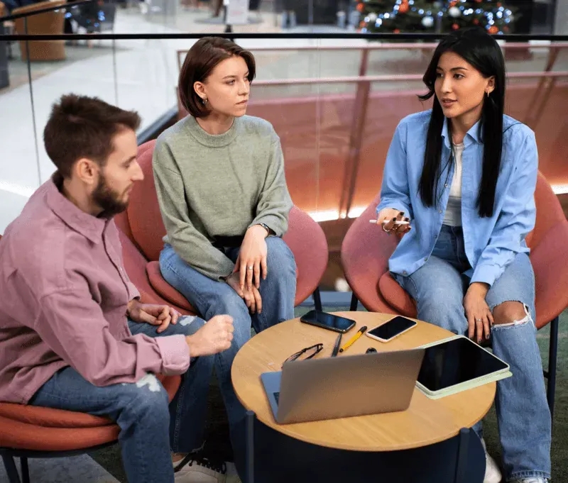 Three colleagues talking through a project around a small table with a laptop and a tablet